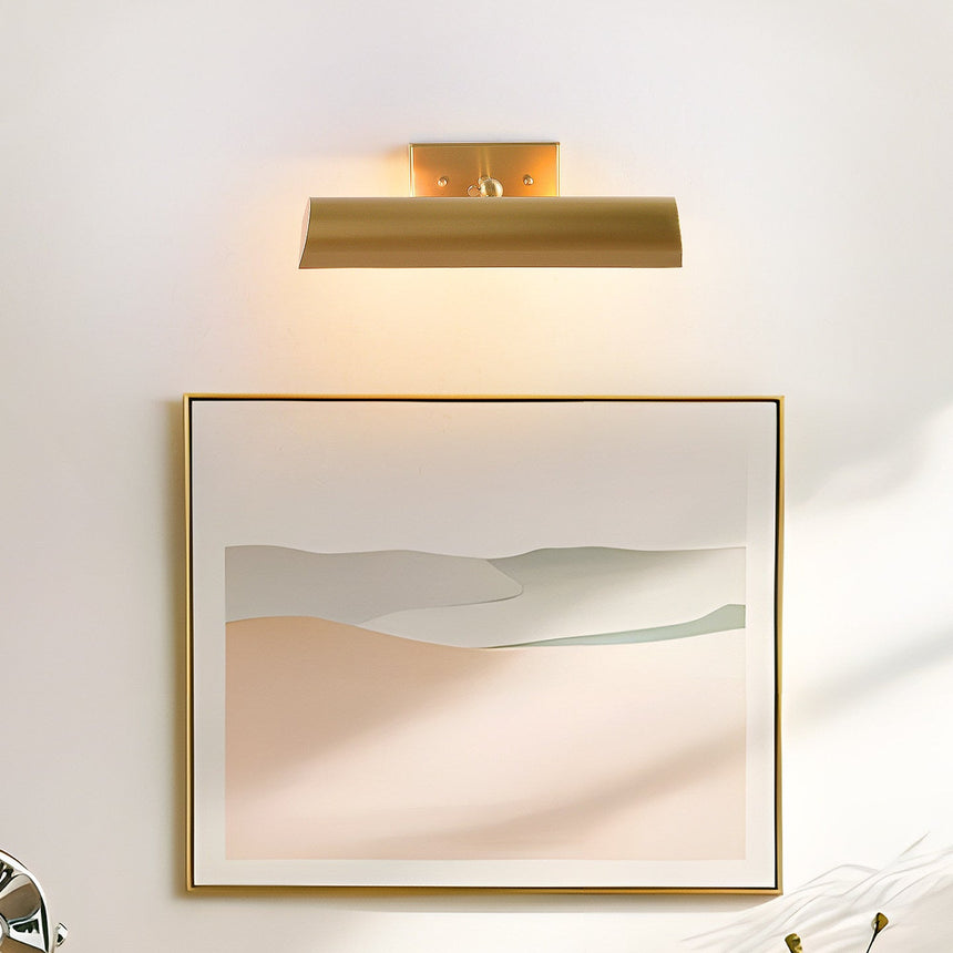Brass shade lit above a framed pale landscape print on a white wall