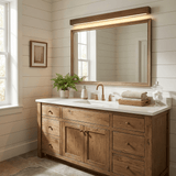 Wood bar lit above a framed mirror over a wood vanity with a plant and towels