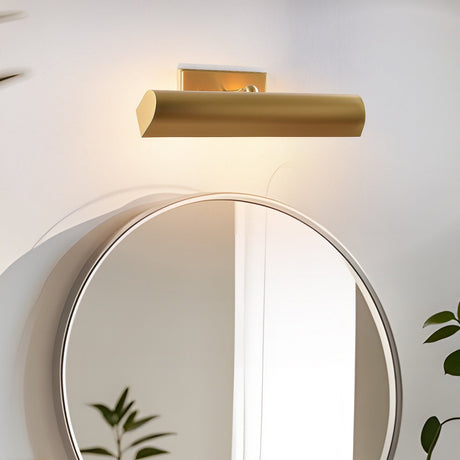 Brass shade lit above a round mirror on a white wall with a plant