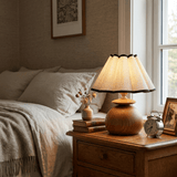 Accent table lamp lit on a nightstand beside a made bed and a clock
