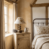 Floral shade lamp lit on a rustic nightstand beside an iron bed
