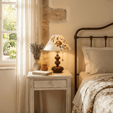Floral shade lamp lit on a white nightstand beside a window
