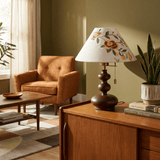 Floral shade lamp lit on a wood desk beside a green wall and a chair