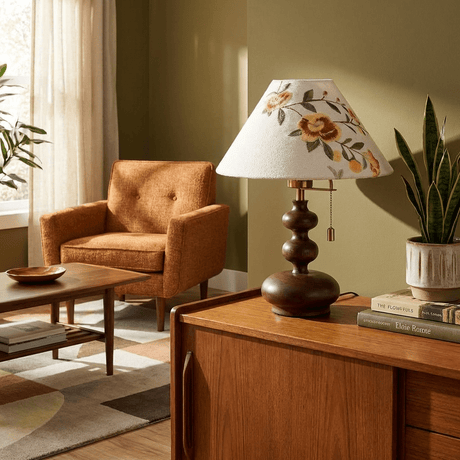 Floral shade lamp lit on a wood desk beside a green wall and a chair