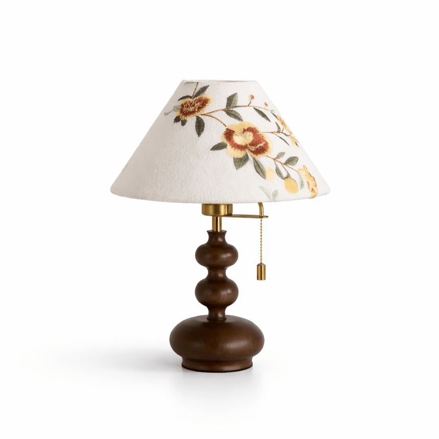 Floral shade lamp lit on a plain ground, the pull chain hanging