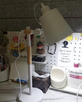 Adjustable desk lamp lit on a desk in front of a wooden pegboard
