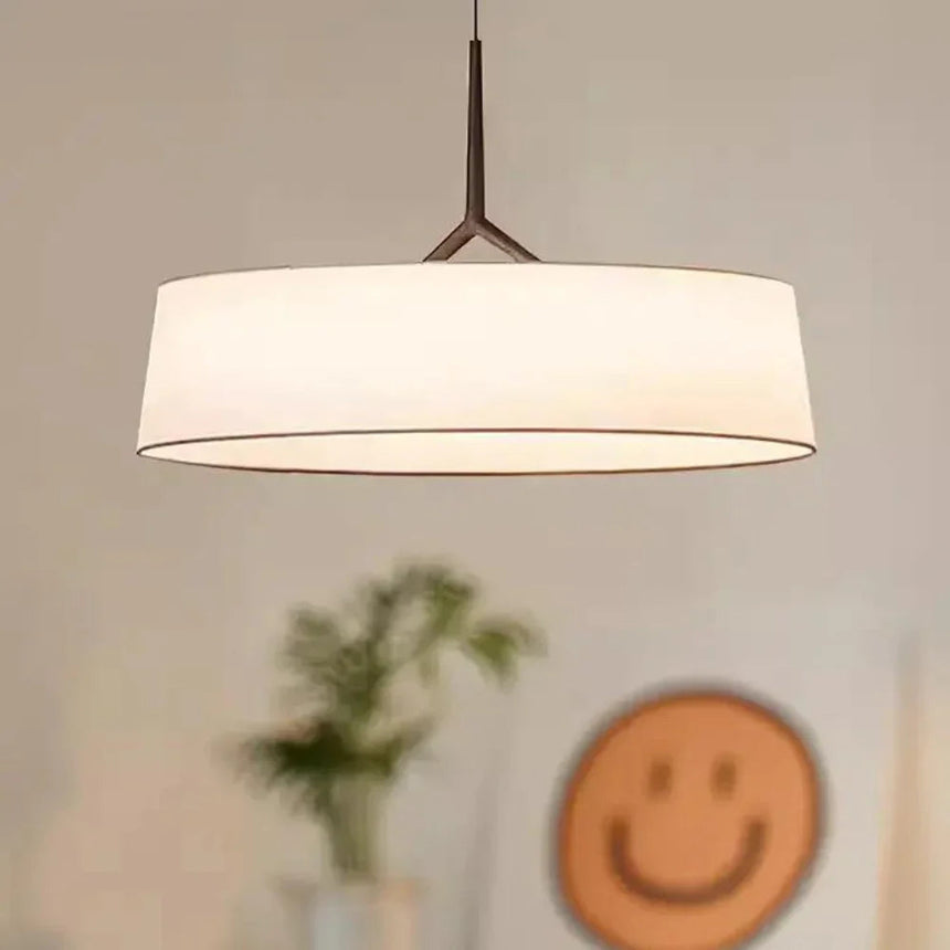 Flat drum shade lit above a table with a small vase