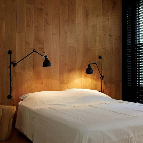 Two swing arm lamps on a wood paneled wall above a bed with white linens
