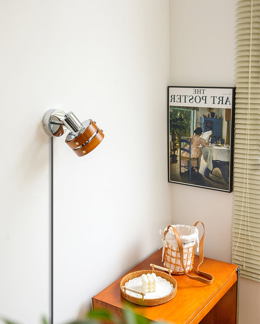 Sconce lit above a small side table with a basket and a framed print