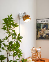 Walnut drum sconce on a wall behind tall green foliage