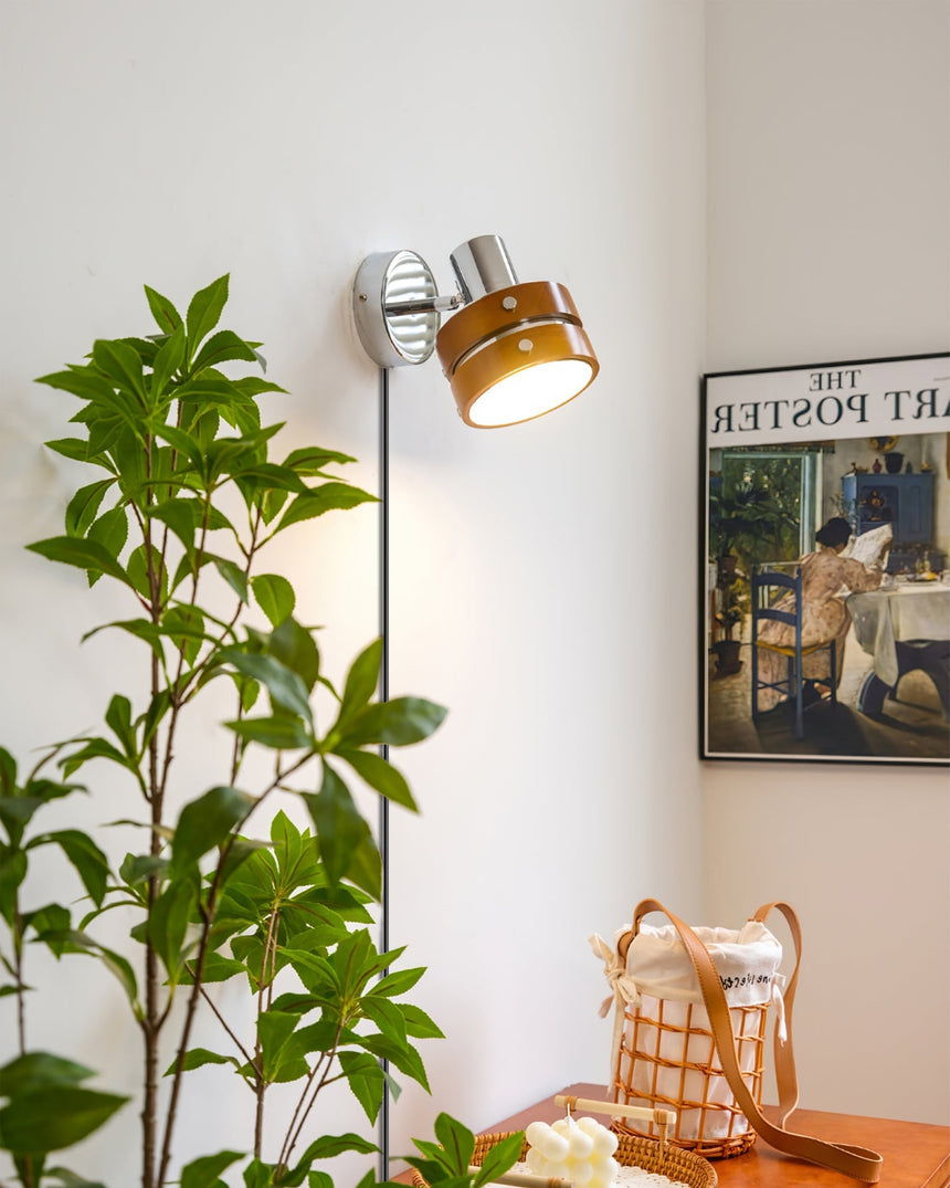 Walnut drum sconce on a wall behind tall green foliage
