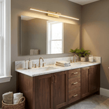 Brass bar lit above a wide mirror over a double basin walnut vanity with a plant
