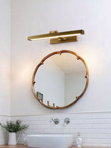 Brass bar lit above a round mirror over a basin with a plant on the counter