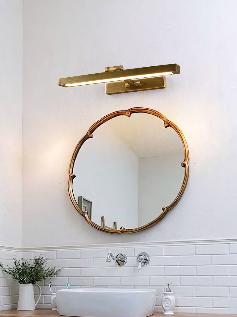 Brass bar lit above a round mirror over a basin with a plant on the counter