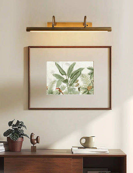 Brass bar lit over a framed botanical print above a walnut desk with a cup