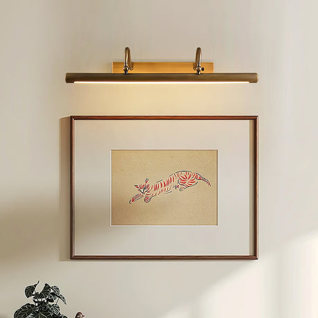Brass bar lit over a framed script print above a plant on a pale wall