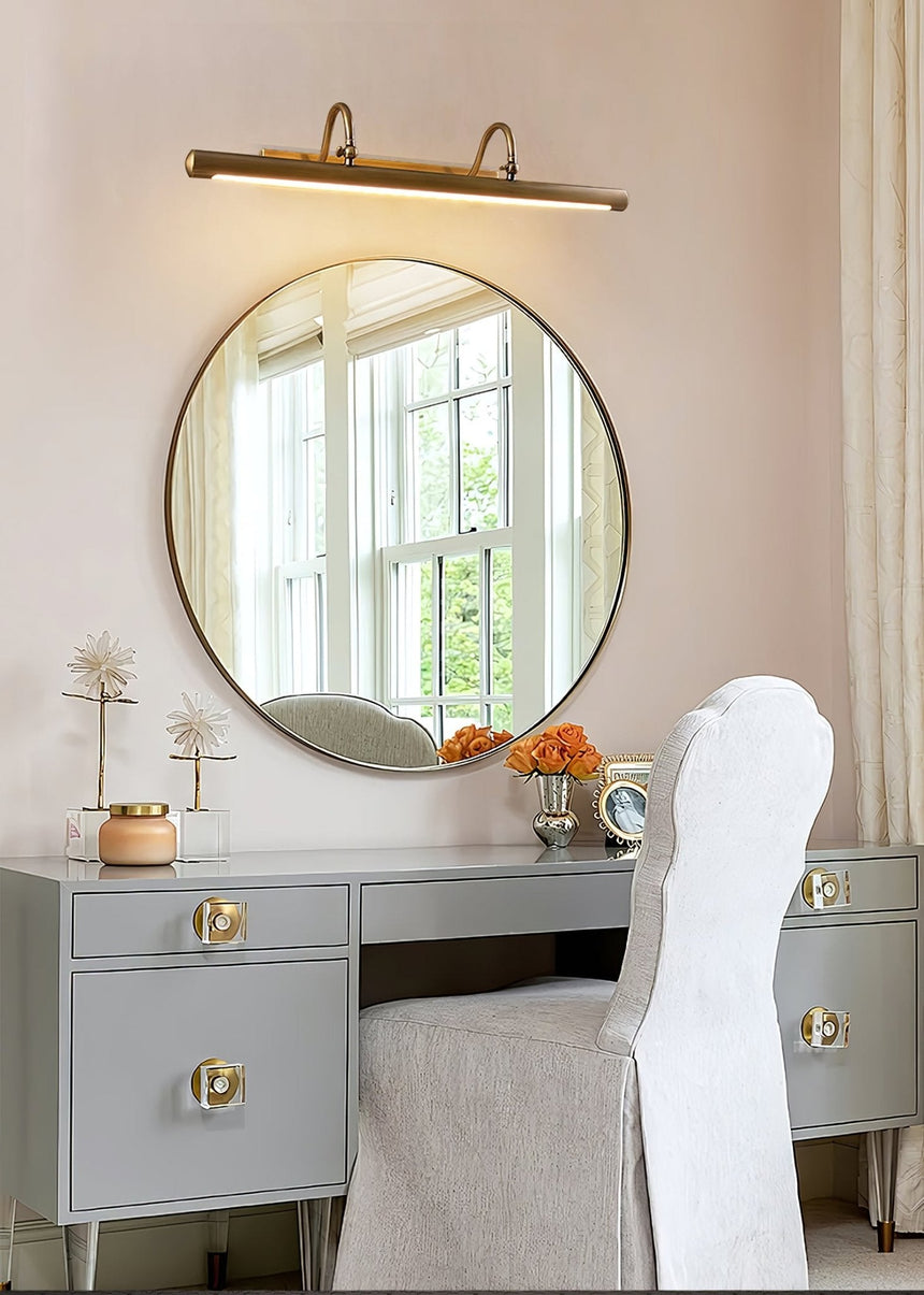 Brass bar above a round mirror on a vanity table with a chair and orange flowers
