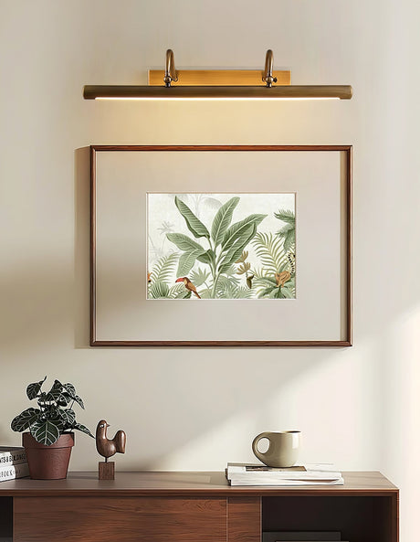 Brass bar lit over a framed botanical print above a walnut console with a plant