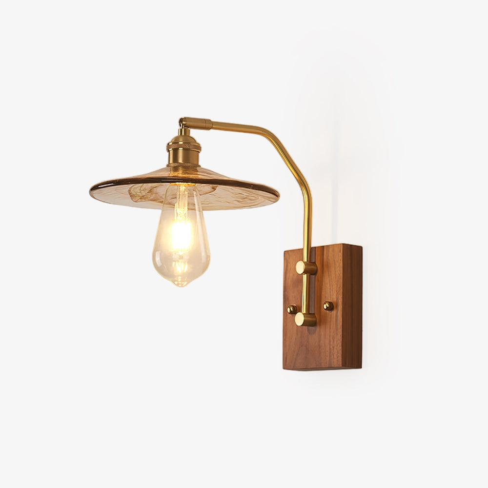 Aged brass wall sconce with a clear glass shade on a walnut backplate