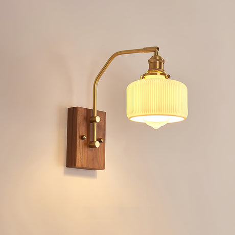 Ribbed opal drum shade lit on a brass arm above a walnut wall plate