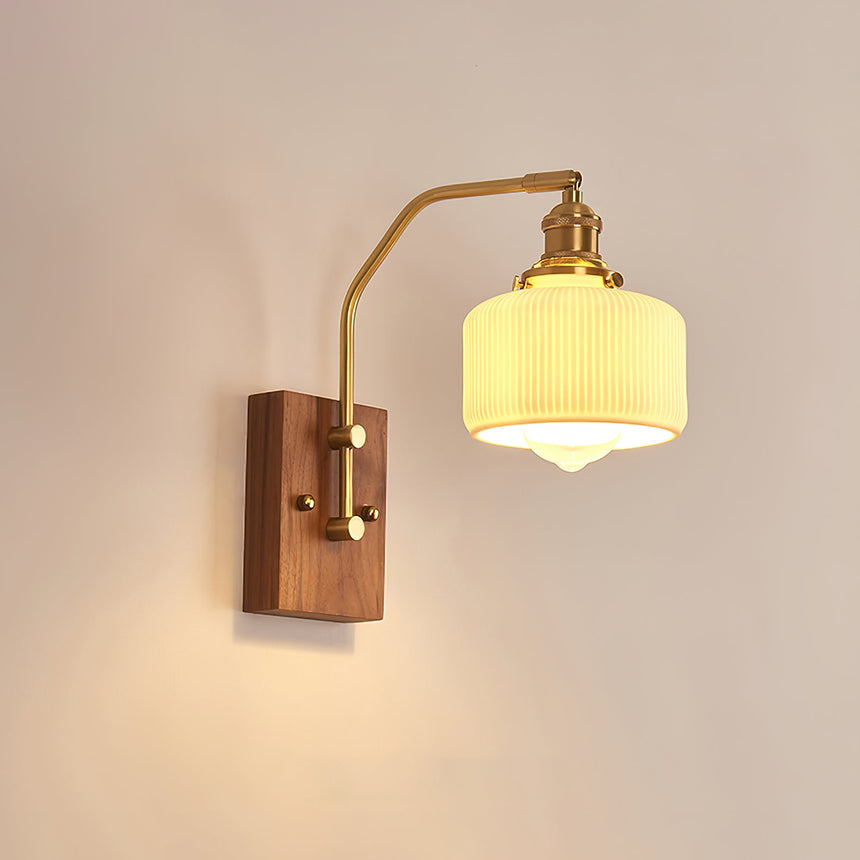 Ribbed opal drum shade lit on a brass arm above a walnut wall plate