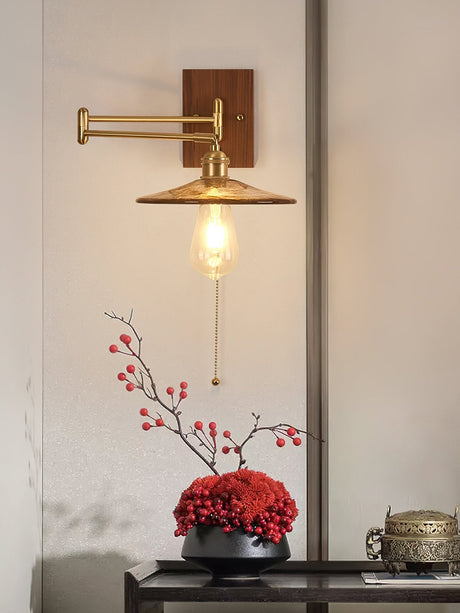 Brass and walnut sconce lit above a console table holding red branches