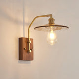 Wide clear glass disc shade lit on a brass arm over a walnut plate
