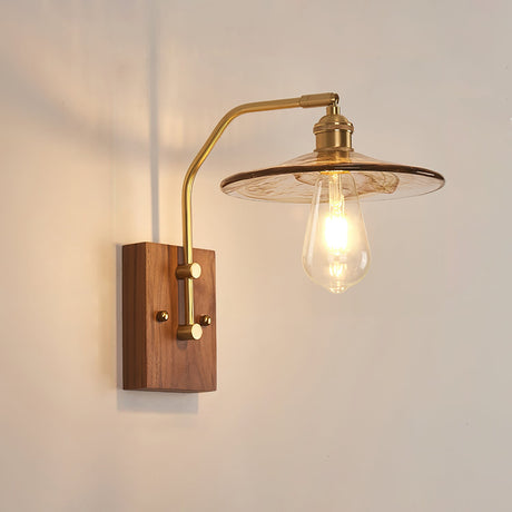 Wide clear glass disc shade lit on a brass arm over a walnut plate