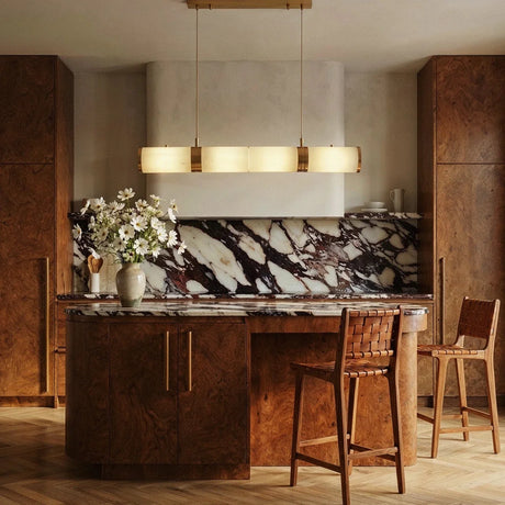 The lit tube above a kitchen island with stools and a marble backsplash