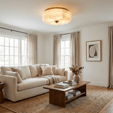 Scalloped alabaster ceiling light lit in a living room with a pale sofa and a rug