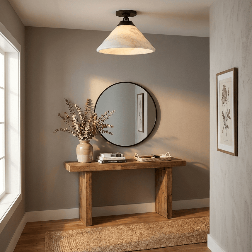 Alabaster cone ceiling light above a console table with a round mirror and dried stems