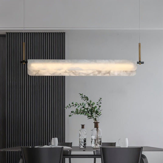 A lit stone bar over a dining table with chairs and a plant beside a slatted wall