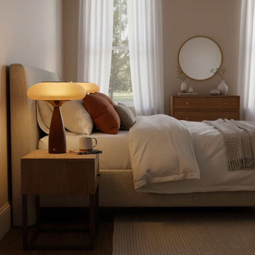 Amber glass table lamp lit on a nightstand beside a made bed