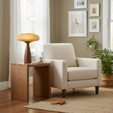 Amber glass table lamp lit on a side table beside a pale armchair