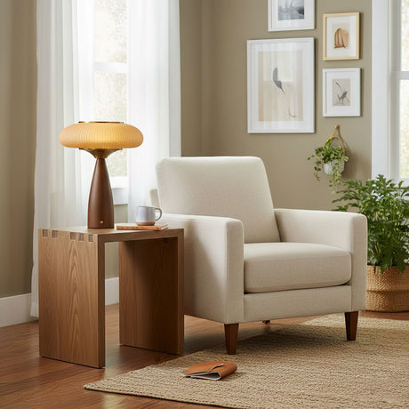 Amber glass table lamp lit on a side table beside a pale armchair