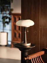White glass table lamp lit on a carved wood stand in a hallway