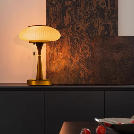 Amber glass table lamp lit on a dark desk against a warm wall
