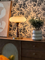 Amber glass table lamp lit on a dresser against a patterned wall