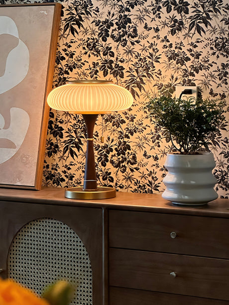 Amber glass table lamp lit on a dresser against a patterned wall