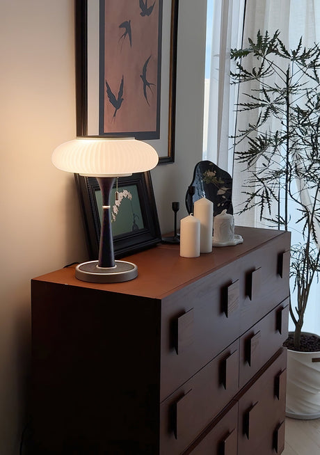 White glass table lamp lit on a red chest beside framed pictures
