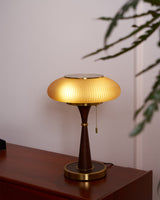 Amber glass table lamp lit on a reddish wood console