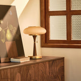 Amber glass table lamp lit on a sideboard beside leaning artwork