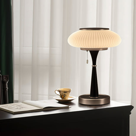 Table lamp with a ribbed glass cap lit beside an open book and a cup