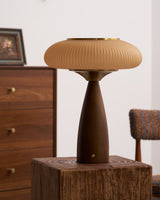 Amber glass table lamp lit on a wooden block beside a chest of drawers