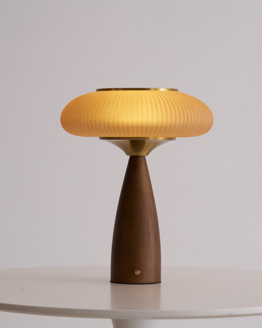 Amber glass table lamp lit and seen from the front on a pale ground