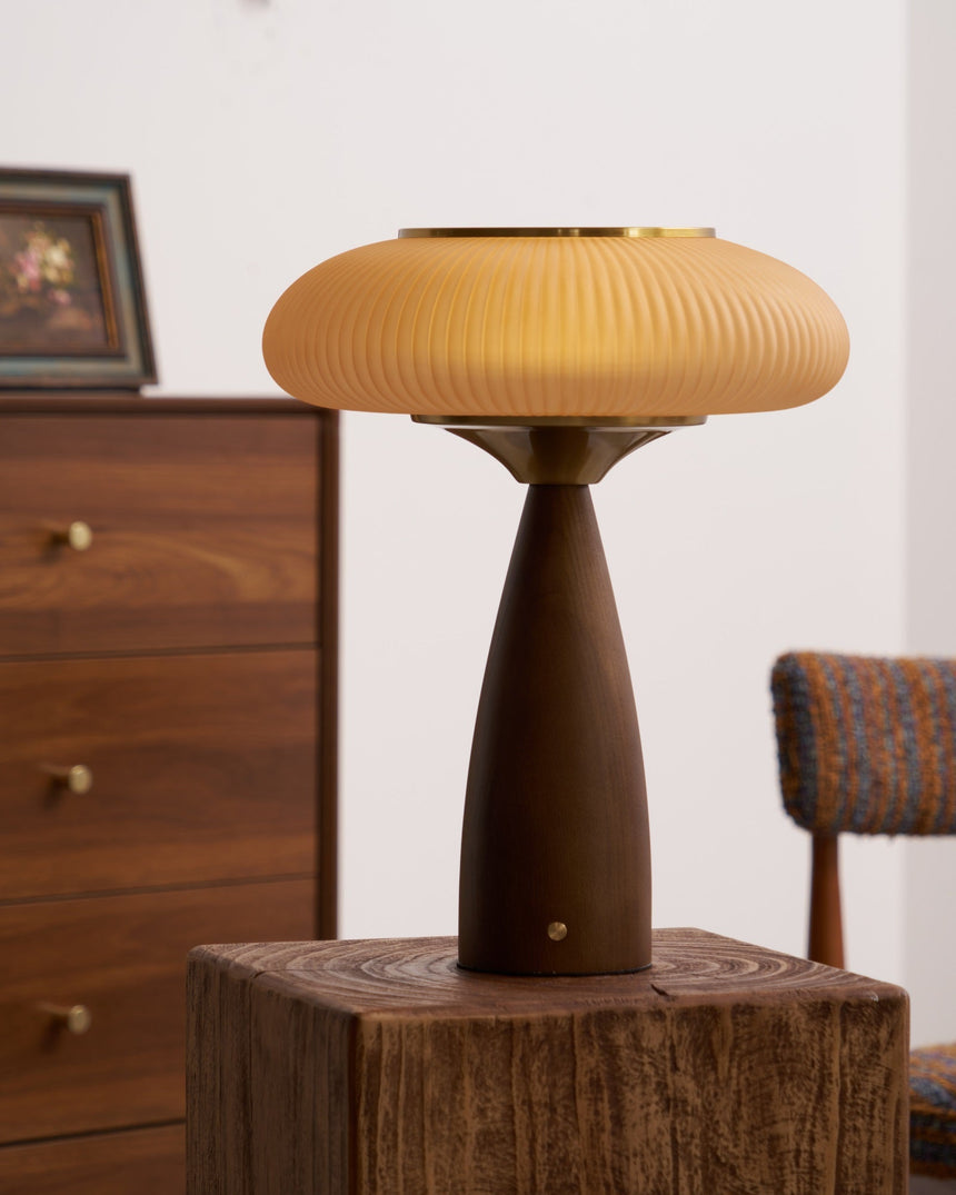 Amber glass table lamp lit on a wooden block in front of a dresser