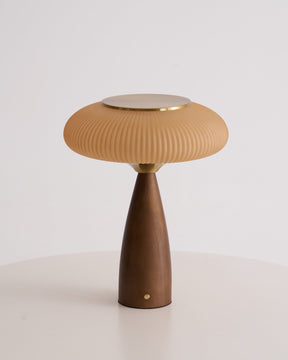 Amber glass table lamp lit and seen in full against a plain ground