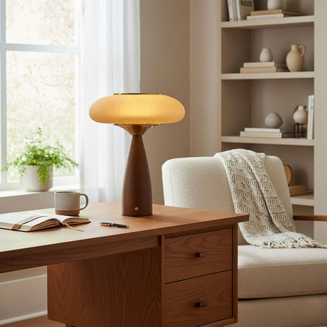 Amber glass table lamp lit on a wooden desk beside a mug and a book