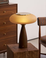 Amber glass table lamp lit on a rough wooden block beside a chair