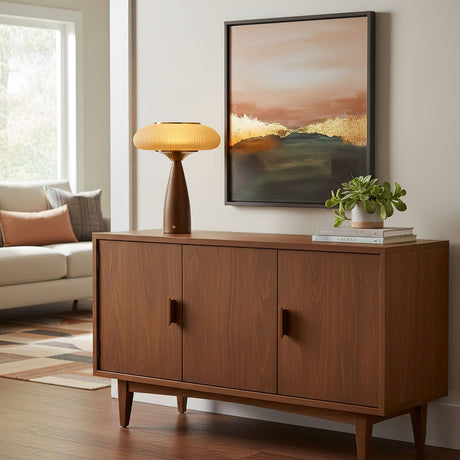 Amber glass table lamp lit on a sideboard below a framed landscape